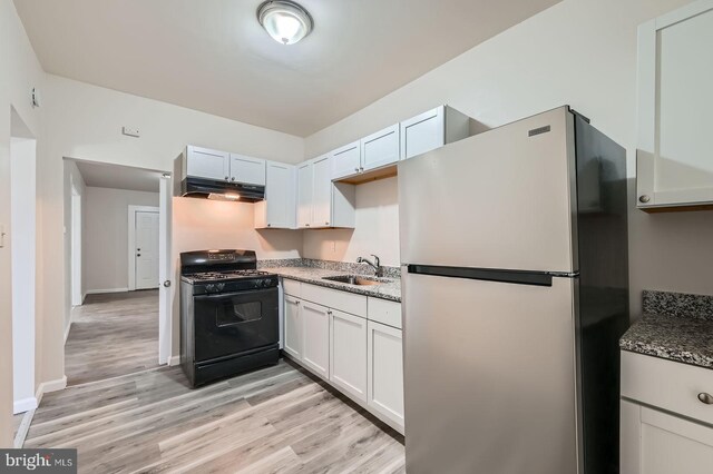 118 N Hilton St, Baltimore, MD 21229 - kitchen with freestanding refrigerator, black range with gas stovetop, under cabinet range hood, a sink, and light wood-style floors