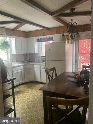 19 S Elberon Ave, Atlantic City, NJ 08401 - kitchen featuring freestanding refrigerator, beam ceiling, a chandelier, white cabinets, and healthy amount of natural light