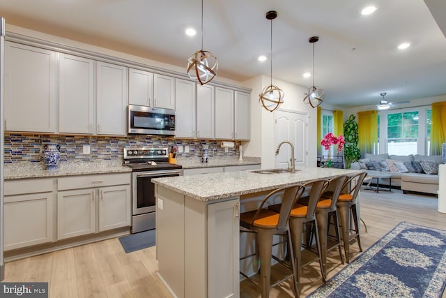 16600 Tortola Dr, Accokeek, MD 20607 - kitchen with stainless steel appliances, a sink, tasteful backsplash, light wood-style flooring, and a center island with sink