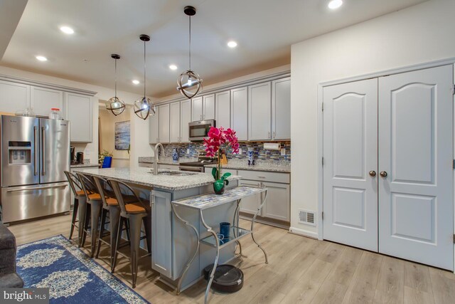16600 Tortola Dr, Accokeek, MD 20607 - kitchen featuring appliances with stainless steel finishes, backsplash, light wood-style flooring, a breakfast bar, and light stone counters
