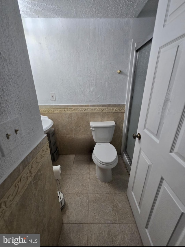 13721 Hobart Dr, Silver Spring, MD 20904 - bathroom with toilet, tile walls, a shower with door, a wainscoted wall, and tile patterned floors