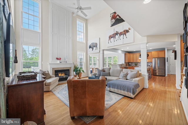 3 Graham Ct, Middletown, DE 19709 - living room featuring a high ceiling, light wood-type flooring, a large fireplace, ceiling fan, and decorative columns