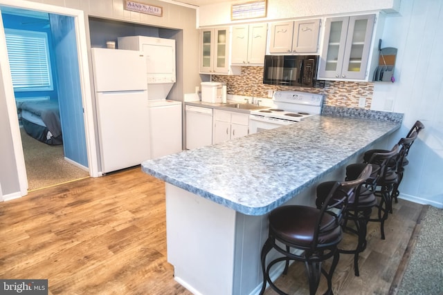 17 139th St Unit 105, Ocean City, MD 21842 - kitchen featuring white appliances, a peninsula, a breakfast bar area, tasteful backsplash, and light wood-style flooring