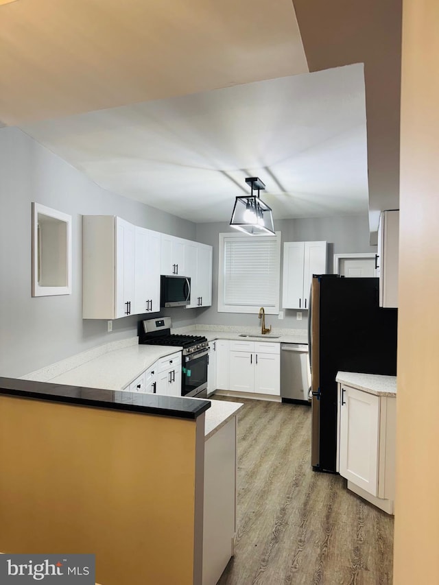 1402 W Saratoga St, Baltimore, MD 21223 - kitchen with appliances with stainless steel finishes, a sink, a peninsula, light wood-type flooring, and white cabinets