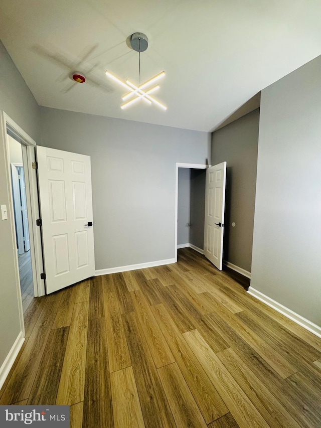 1402 W Saratoga St, Baltimore, MD 21223 - unfurnished bedroom with wood finished floors, a chandelier, and baseboards