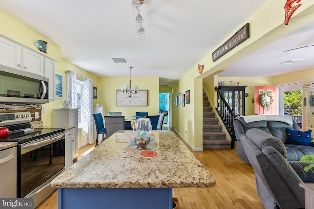 25 N 12th St, Del Haven, NJ 08251 - kitchen with appliances with stainless steel finishes, open floor plan, a chandelier, white cabinetry, and light stone countertops