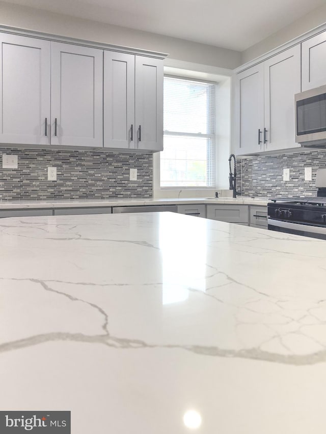 1736 E 30th St, Baltimore, MD 21218 - kitchen featuring stainless steel microwave, decorative backsplash, gas stove, light stone counters, and gray cabinets