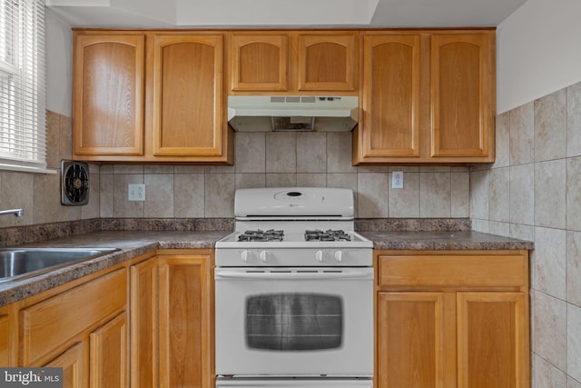210 Erica Ter, Philadelphia, PA 19116 - kitchen with white gas range, under cabinet range hood, a sink, dark countertops, and backsplash