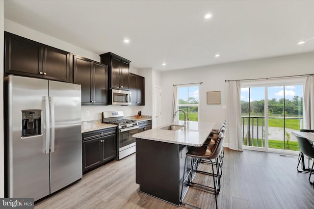 118 Fletcher Cir, Middletown, DE 19709 - kitchen with stainless steel appliances, a sink, light wood-style floors, light stone countertops, and a kitchen island with sink