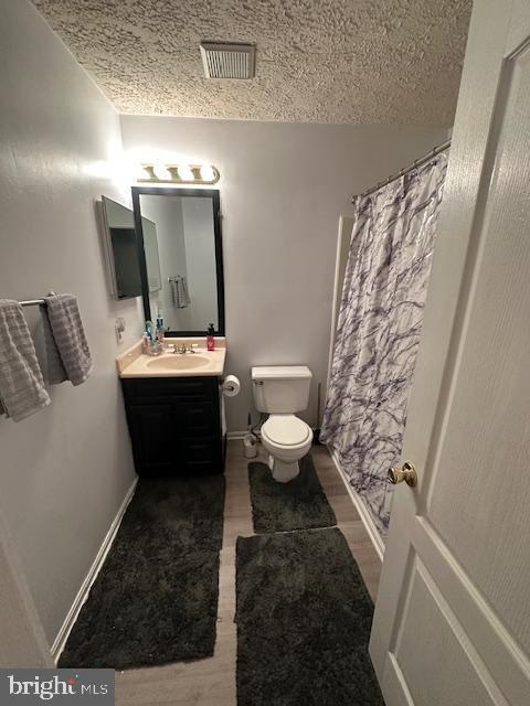 6708 Pauline Ct, Bryans Road, MD 20616 - full bath featuring toilet, vanity, curtained shower, wood finished floors, and a textured ceiling