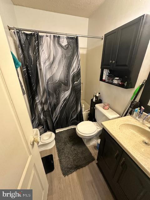 6708 Pauline Ct, Bryans Road, MD 20616 - bathroom with vanity, wood finished floors, toilet, a textured ceiling, and shower / tub combo with curtain
