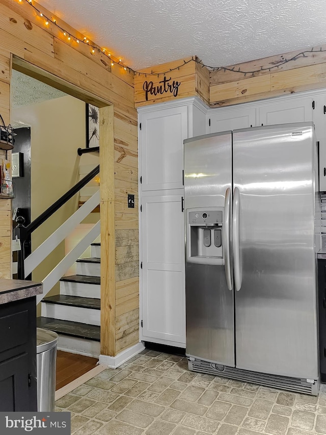 24950 Morgan Rd, Hollywood, MD 20636 - kitchen with stainless steel refrigerator with ice dispenser, wooden walls, a textured ceiling, white cabinetry, and baseboards