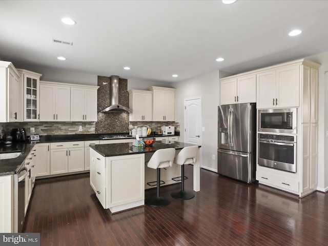 42350 Stonemont Cir, Ashburn, VA 20148 - kitchen featuring wall chimney range hood, appliances with stainless steel finishes, a center island, tasteful backsplash, and glass insert cabinets