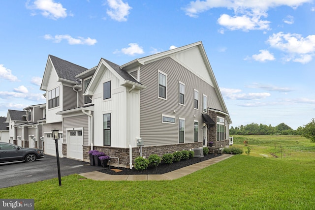 71 Tamarack Cir, Eagleville, PA 19403 - view of side of home featuring stone siding, an attached garage, driveway, a lawn, and cooling unit