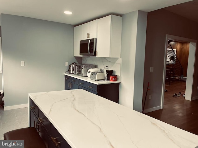 123 Bryn Mawr Ave, Bala Cynwyd, PA 19004 - kitchen featuring stainless steel microwave, light stone countertops, backsplash, baseboards, and white cabinets