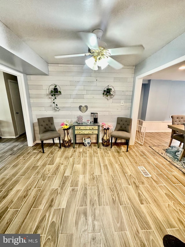 12403 Rambling Ln, Bowie, MD 20715 - sitting room featuring light wood-type flooring, a ceiling fan, a textured ceiling, baseboards, and wooden walls