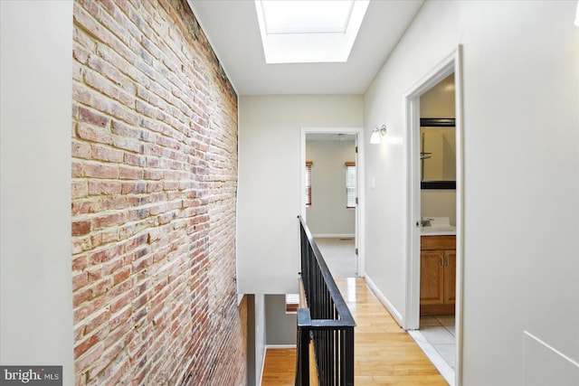 1225 W Cross St, Baltimore, MD 21230 - hallway with brick wall, light wood finished floors, an upstairs landing, a skylight, and baseboards