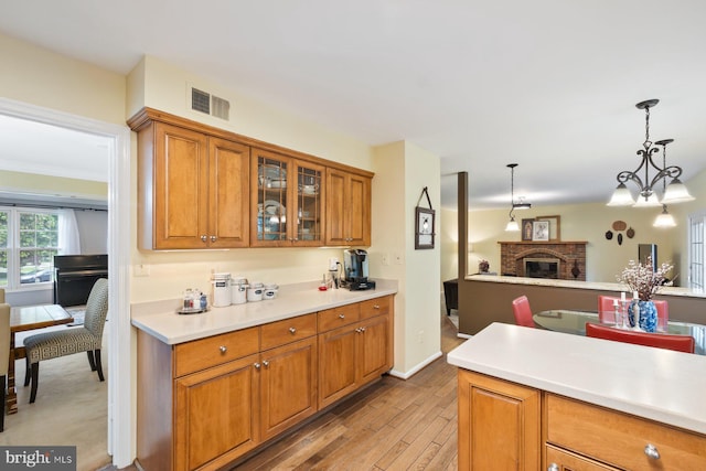 9300 Olivia Pl, Burke, VA 22015 - kitchen featuring brown cabinetry, light wood finished floors, light countertops, glass insert cabinets, and decorative light fixtures