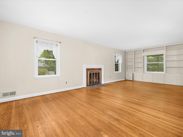 6748 Glenkirk Rd, Baltimore, MD 21239 - unfurnished living room featuring light wood-style floors, built in shelves, a brick fireplace, and baseboards