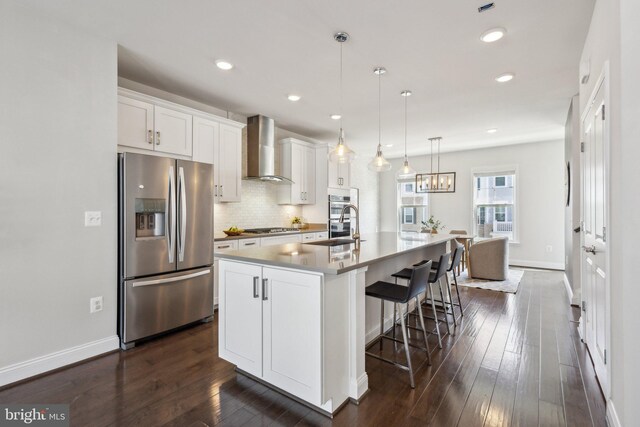 1909 Greenbriar Hall Rd, Dumfries, VA 22026 - kitchen featuring appliances with stainless steel finishes, wall chimney exhaust hood, a center island with sink, white cabinets, and a breakfast bar