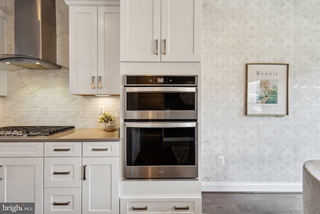1909 Greenbriar Hall Rd, Dumfries, VA 22026 - kitchen featuring wall chimney range hood, appliances with stainless steel finishes, wood finished floors, white cabinets, and decorative backsplash