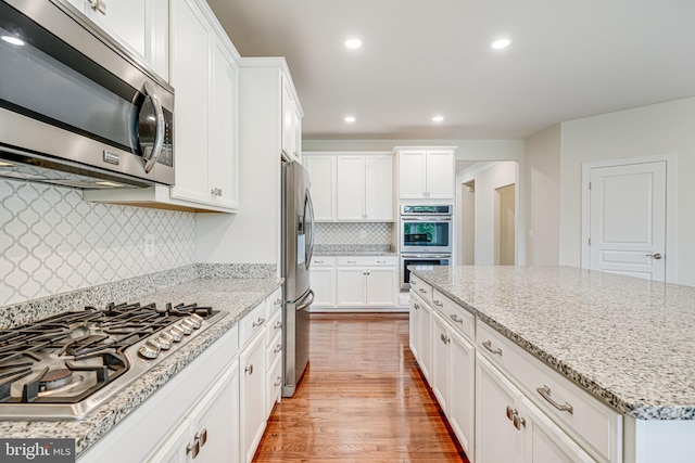 7425 Signal Hill Rd, Manassas, VA 20111 - kitchen featuring stainless steel appliances, light wood finished floors, white cabinetry, backsplash, and light stone counters