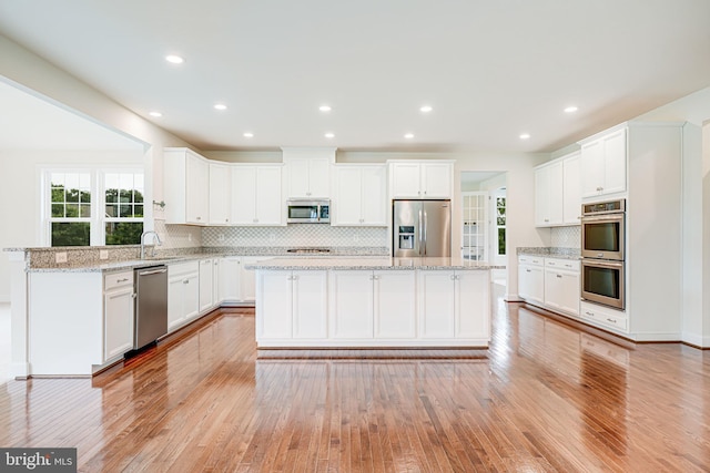 7425 Signal Hill Rd, Manassas, VA 20111 - kitchen featuring appliances with stainless steel finishes, light wood-style floors, a center island, tasteful backsplash, and white cabinets