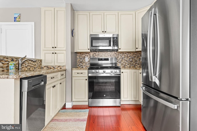 808 Scotia Rd, Philadelphia, PA 19128 - kitchen featuring appliances with stainless steel finishes, cream cabinets, dark wood-style floors, light stone counters, and decorative backsplash