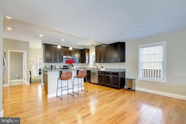 4001 7th St, North Beach, MD 20714 - kitchen featuring stainless steel appliances, a kitchen bar, dark brown cabinetry, light wood-style flooring, and baseboards