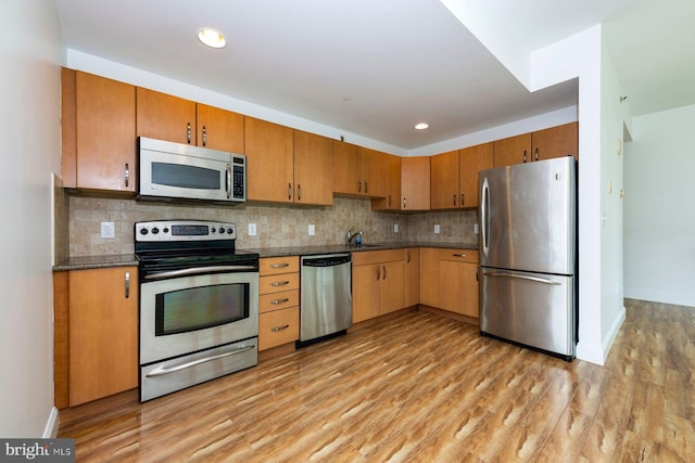 901 N Penn St Unit R305, Philadelphia, PA 19123 - kitchen with stainless steel appliances, light wood-style flooring, dark countertops, a sink, and decorative backsplash