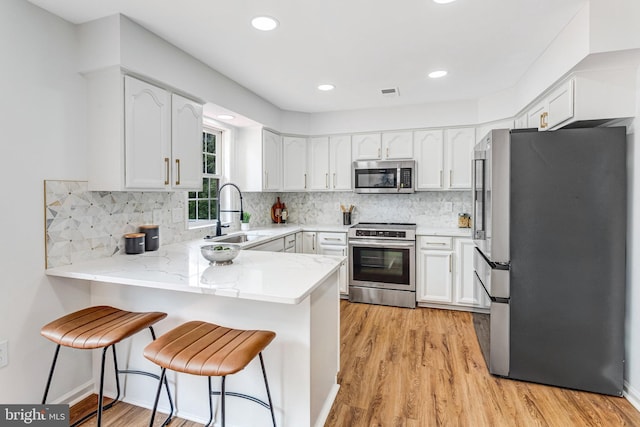 9509 Lincoln Ave, Manassas, VA 20110 - kitchen featuring appliances with stainless steel finishes, a sink, a peninsula, light wood finished floors, and white cabinetry