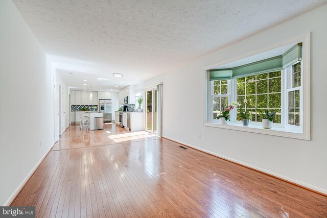 1434 Cellar Creek Way, Herndon, VA 20170 - unfurnished living room featuring healthy amount of natural light, light wood finished floors, baseboards, and a textured ceiling