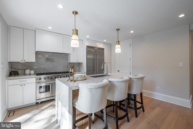 6040 Nebraska Ave NW, Washington, DC 20015 - kitchen featuring high end appliances, a sink, white cabinets, an island with sink, and light wood-style floors