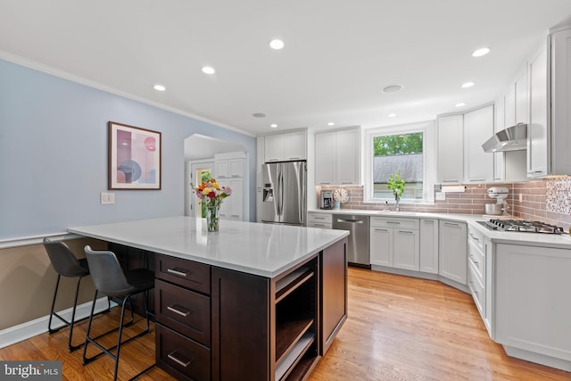 1110 Clover Hill Rd, Wynnewood, PA 19096 - kitchen featuring appliances with stainless steel finishes, under cabinet range hood, light countertops, backsplash, and a kitchen breakfast bar
