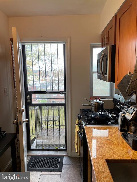 3936 NE Blaine St NE, Washington, DC 20019 - kitchen with stainless steel microwave, gas stove, brown cabinets, light stone countertops, and tile patterned flooring