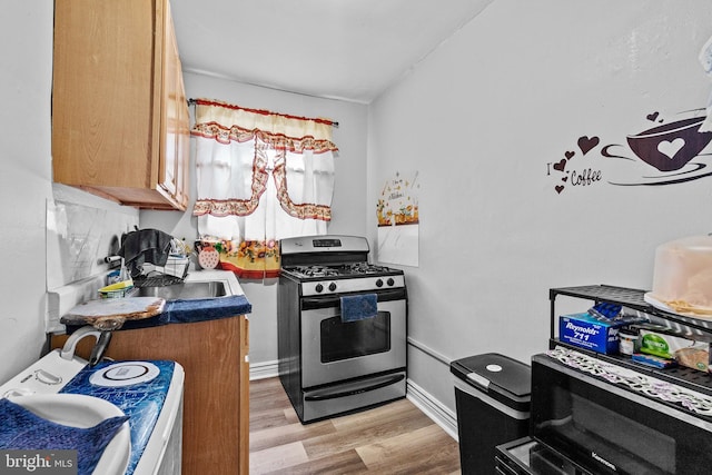 821 E Jeffrey St, Baltimore, MD 21225 - kitchen with stainless steel gas range oven, a sink, light wood finished floors, brown cabinetry, and black microwave