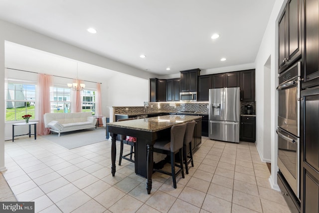 25541 Emerson Oaks Dr, Aldie, VA 20105 - kitchen featuring appliances with stainless steel finishes, decorative backsplash, a chandelier, a kitchen bar, and stone counters
