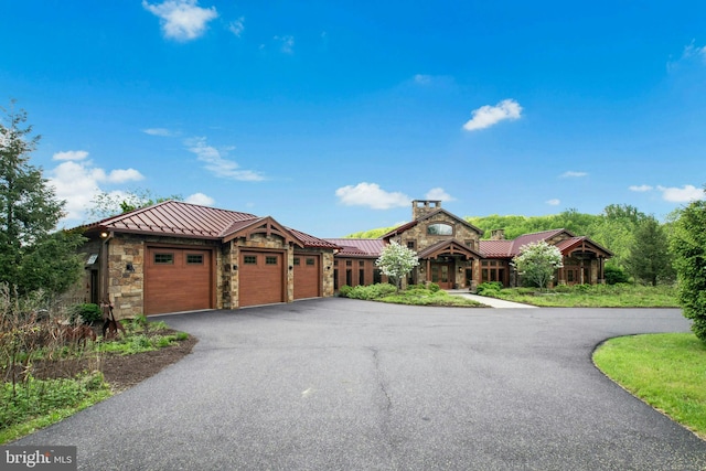2042 Folk Rd, Fogelsville, PA 18051 - view of front of house with a standing seam roof, stone siding, asphalt driveway, an attached garage, and a chimney