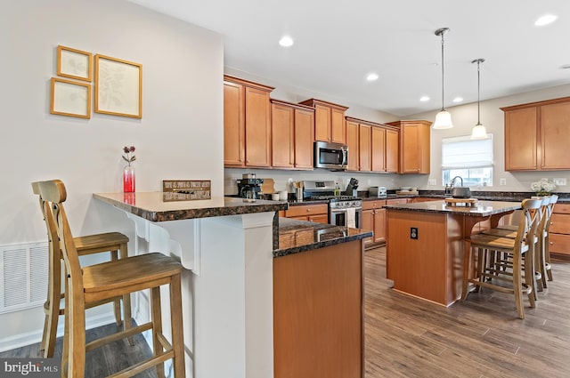 1022 Linden Dr, Hanover, MD 21076 - kitchen featuring appliances with stainless steel finishes, a breakfast bar area, a peninsula, brown cabinets, and hanging light fixtures