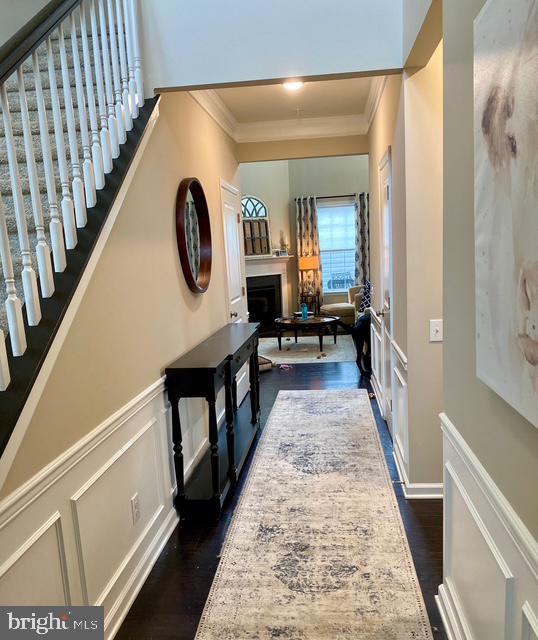 734 Sun Valley Ct, Chester Springs, PA 19425 - hallway with crown molding, a decorative wall, dark wood-style flooring, stairs, and wainscoting