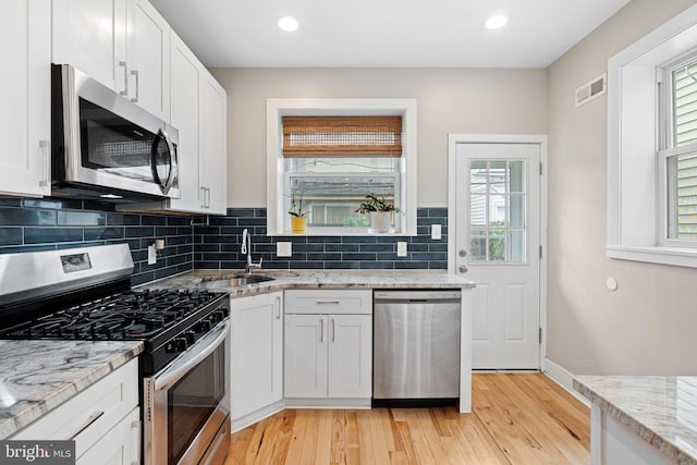 2409 S Watts St, Philadelphia, PA 19148 - kitchen featuring appliances with stainless steel finishes, a sink, light wood finished floors, decorative backsplash, and white cabinetry