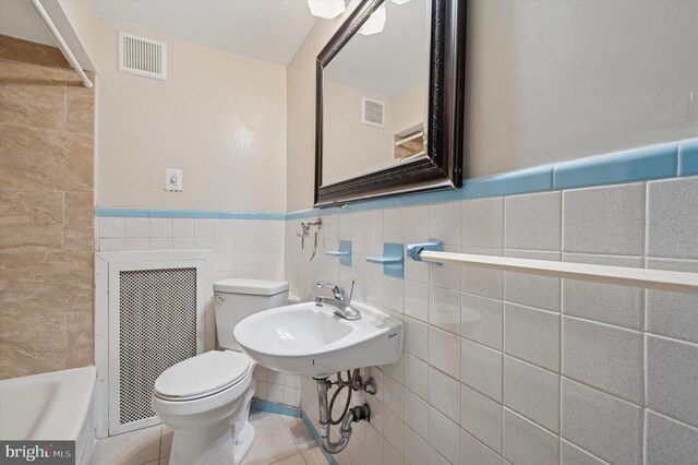 913 Tasker St, Philadelphia, PA 19148 - bathroom featuring toilet, a tub to relax in, tile walls, a sink, and wainscoting