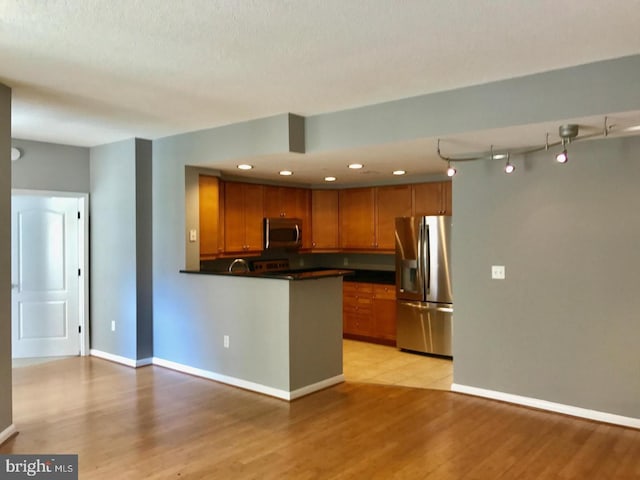 1111 11th St NW Unit 307, Washington, DC 20001 - kitchen with appliances with stainless steel finishes, brown cabinets, dark countertops, a peninsula, and light wood-style flooring