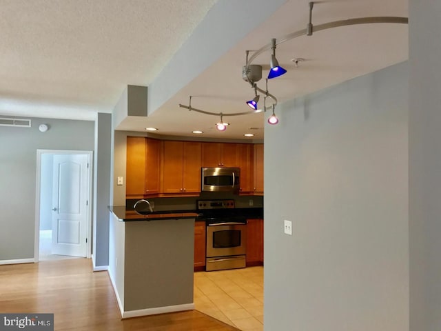 1111 11th St NW Unit 307, Washington, DC 20001 - kitchen featuring stainless steel appliances, dark countertops, a sink, brown cabinetry, and a peninsula