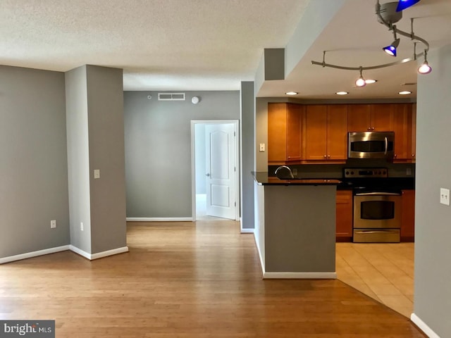 1111 11th St NW Unit 307, Washington, DC 20001 - kitchen with appliances with stainless steel finishes, dark countertops, light wood-style floors, brown cabinets, and baseboards