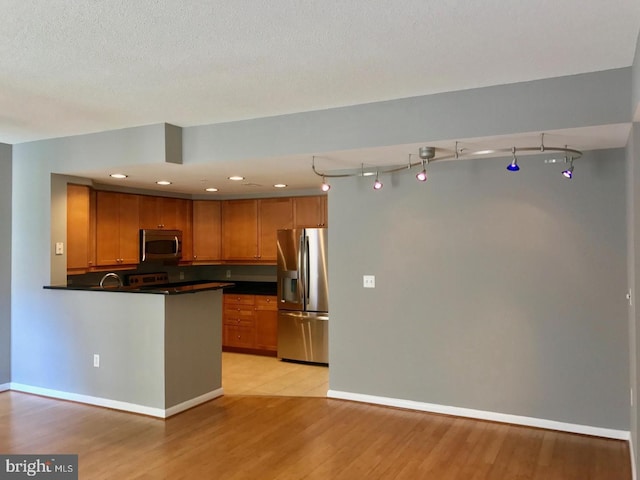 1111 11th St NW Unit 307, Washington, DC 20001 - kitchen featuring stainless steel appliances, dark countertops, brown cabinets, light wood-style floors, and a peninsula