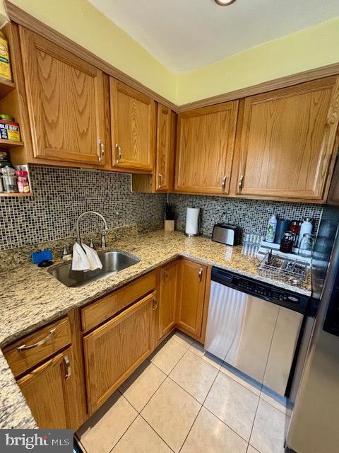 4116 Ellis St, Capitol Heights, MD 20743 - kitchen featuring stainless steel dishwasher, brown cabinets, light tile patterned flooring, light stone counters, and backsplash