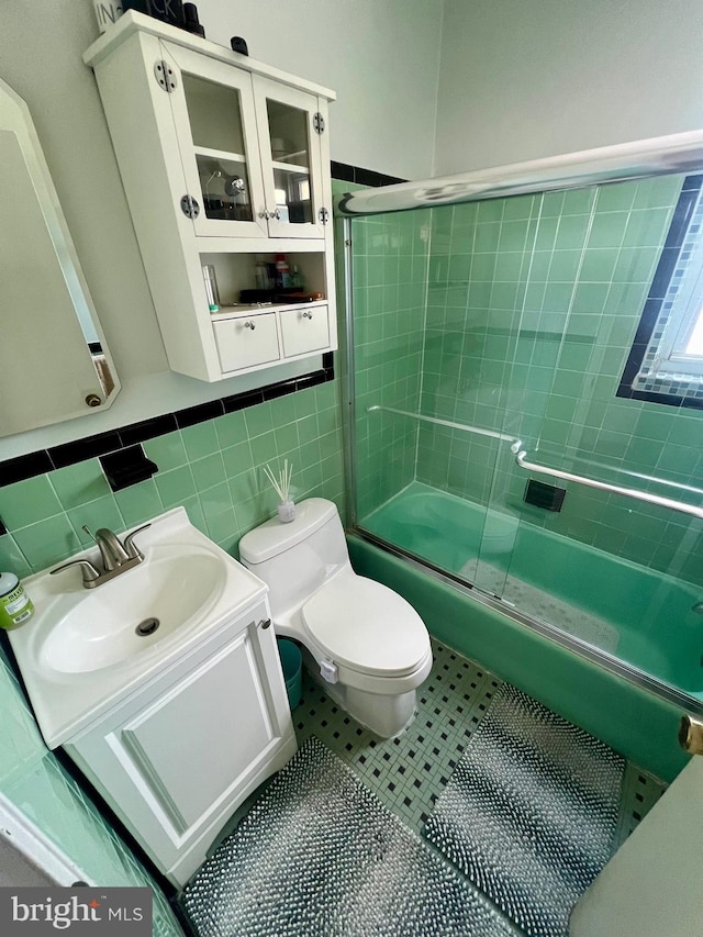 4116 Ellis St, Capitol Heights, MD 20743 - bathroom featuring tile walls, bath / shower combo with glass door, toilet, vanity, and a wainscoted wall