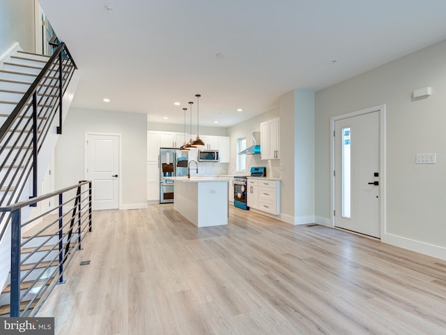 632 Moyer St, Philadelphia, PA 19125 - kitchen with stainless steel appliances, wall chimney exhaust hood, light countertops, a center island with sink, and light wood finished floors