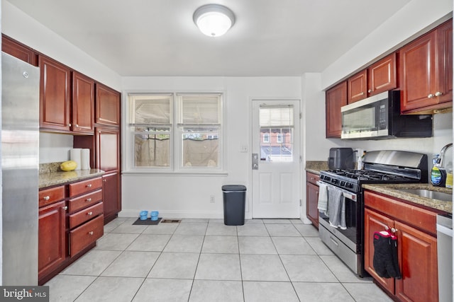 6904 Bank St, Baltimore, MD 21224 - kitchen with stainless steel appliances, reddish brown cabinets, and light tile patterned floors